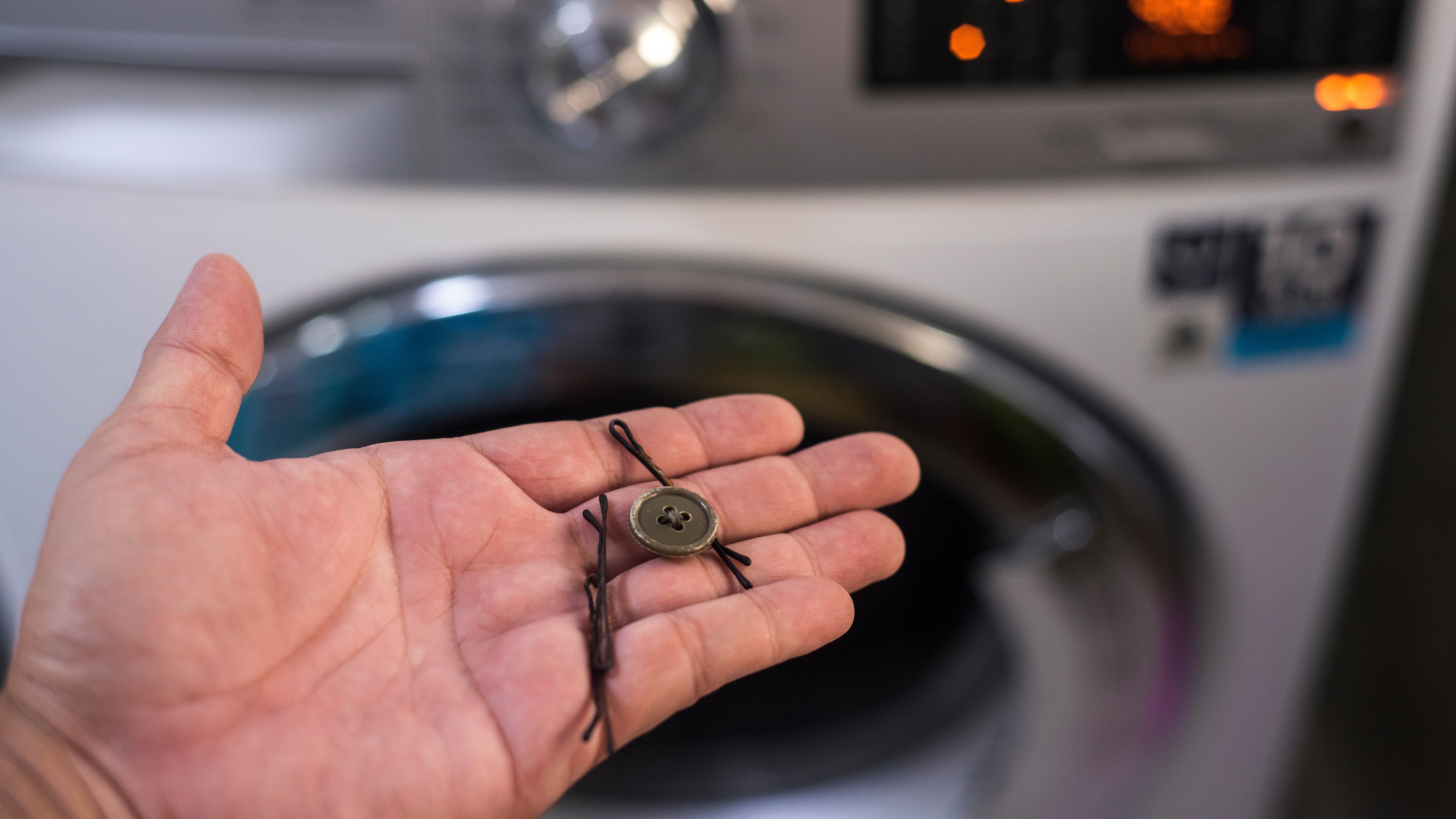Çamaşır makinesinin önünde saç tokası ve düğme tutan biri