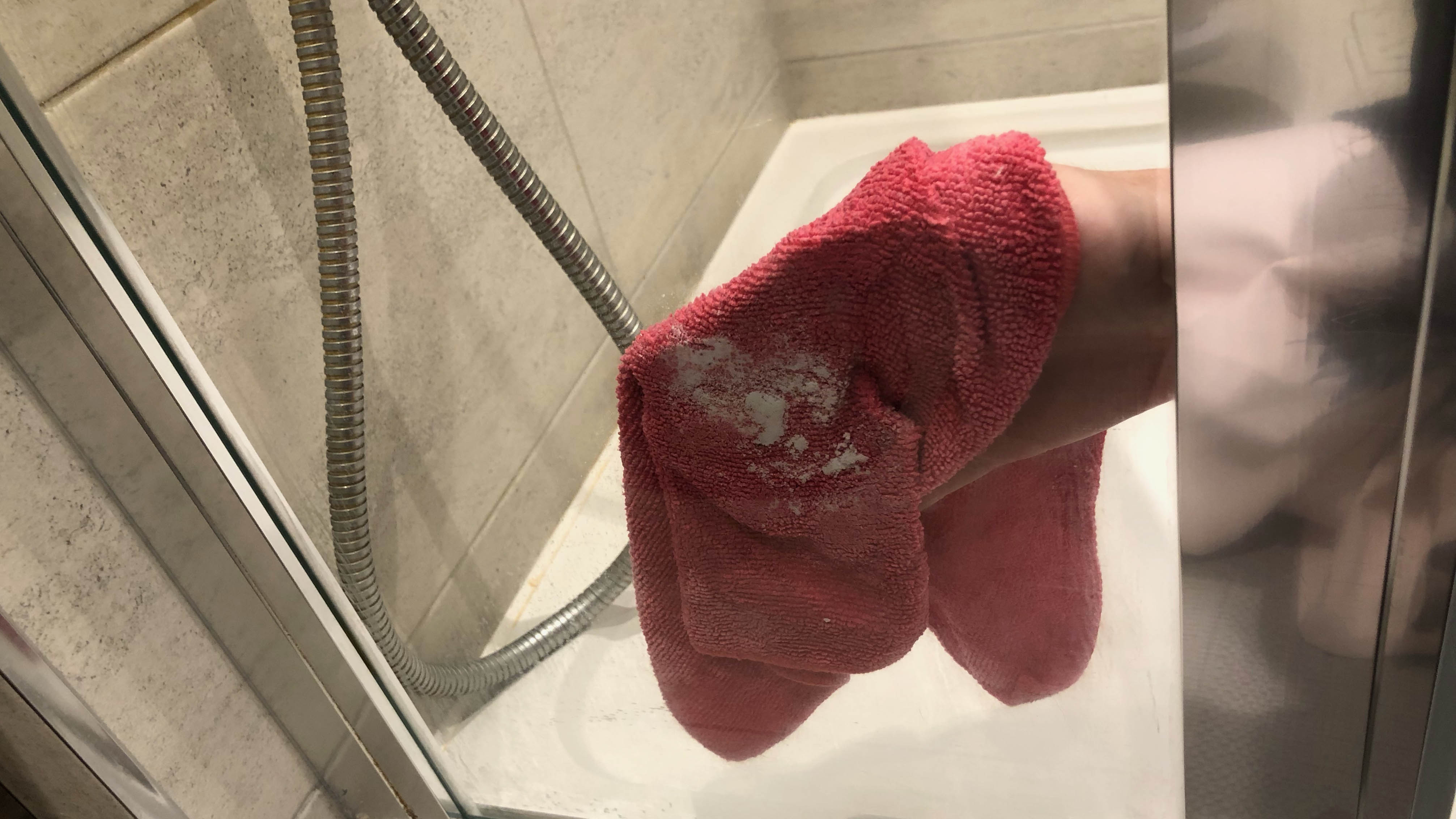 Birisi nemli bir mikrofiber bez üzerinde bir cam duş panelini kabartma tozuyla temizliyor.