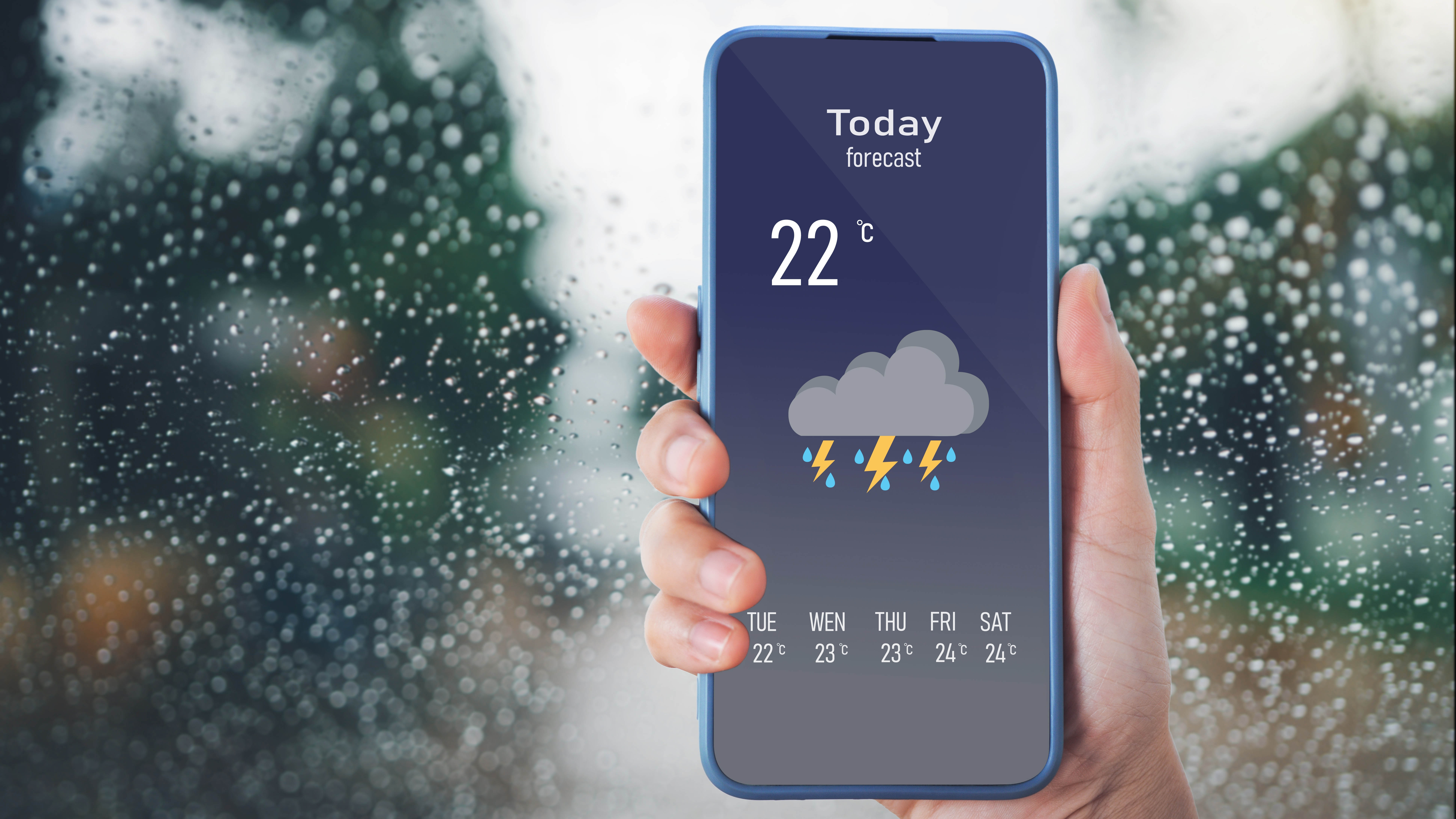 Yağmurla kaplı bir pencerenin önünde planlı gök gürültülü fırtınalı bir hava durumu uygulamasını gösteren bir telefon