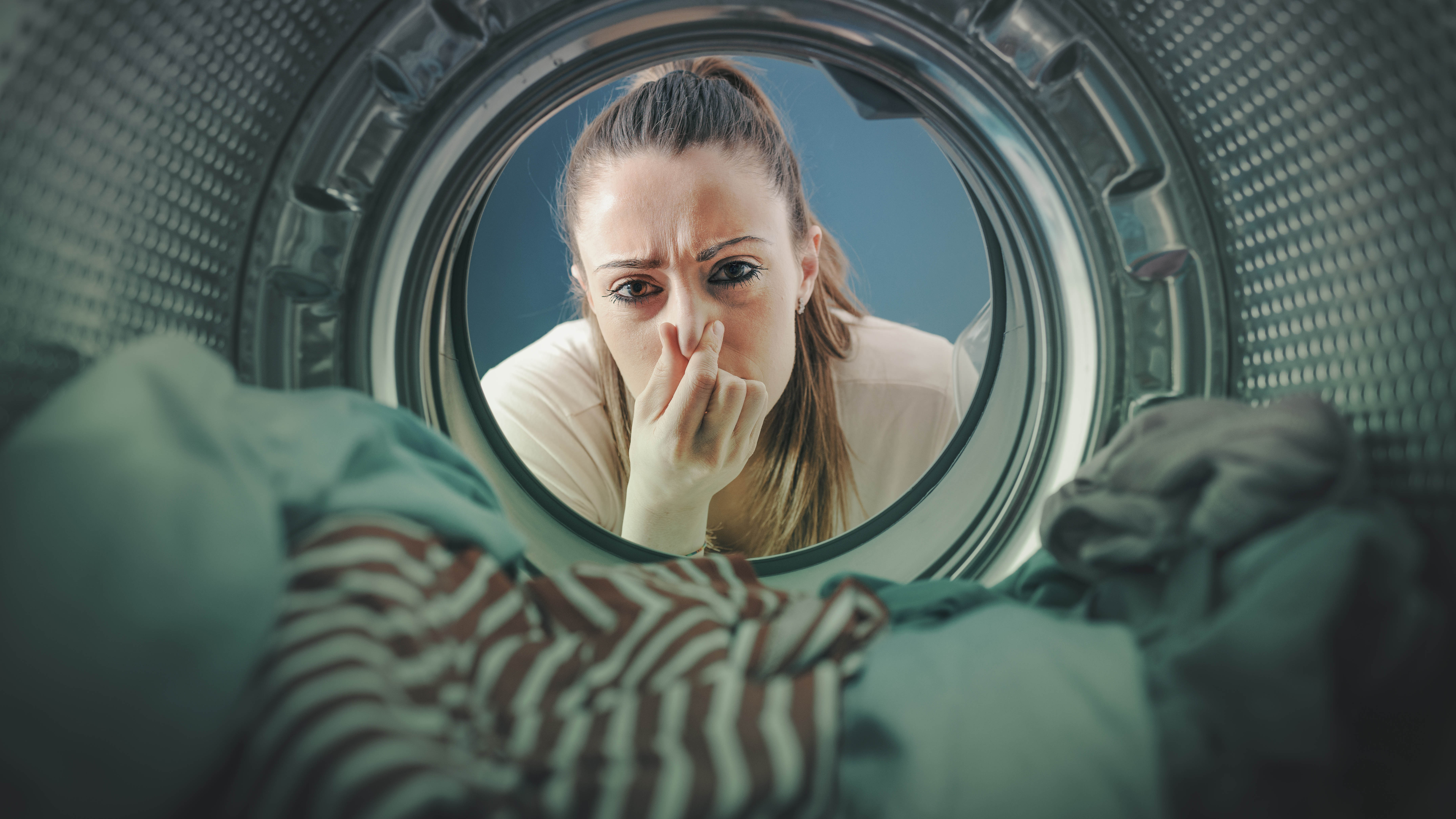 Çamaşır makinesinin içindeki çamaşırlara bakarken burnunu tutan bir kadın.