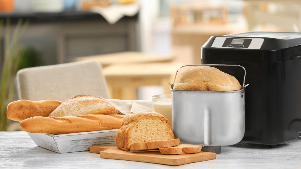 A bread machine next to freshly baked bread on a countertop